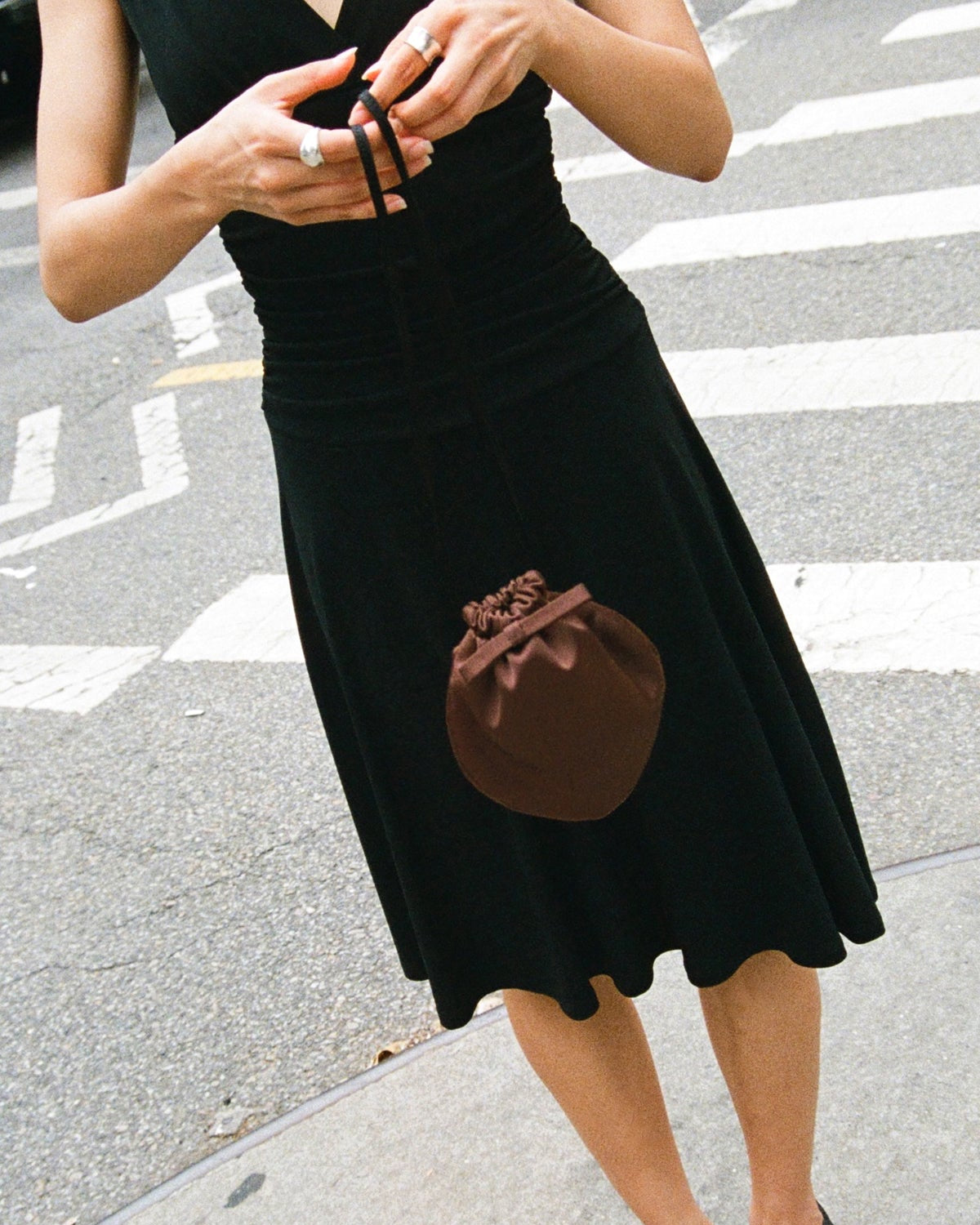 Person wearing a black dress with a brown pocket on a street.