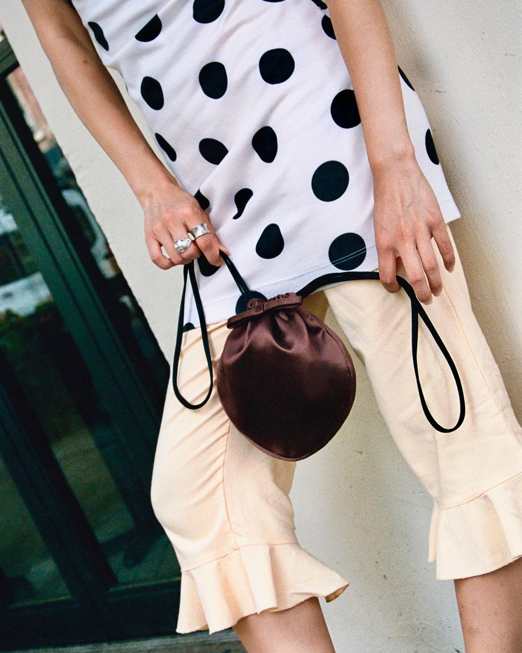 Person wearing a polka dot dress and beige pants holding a brown drawstring bag.