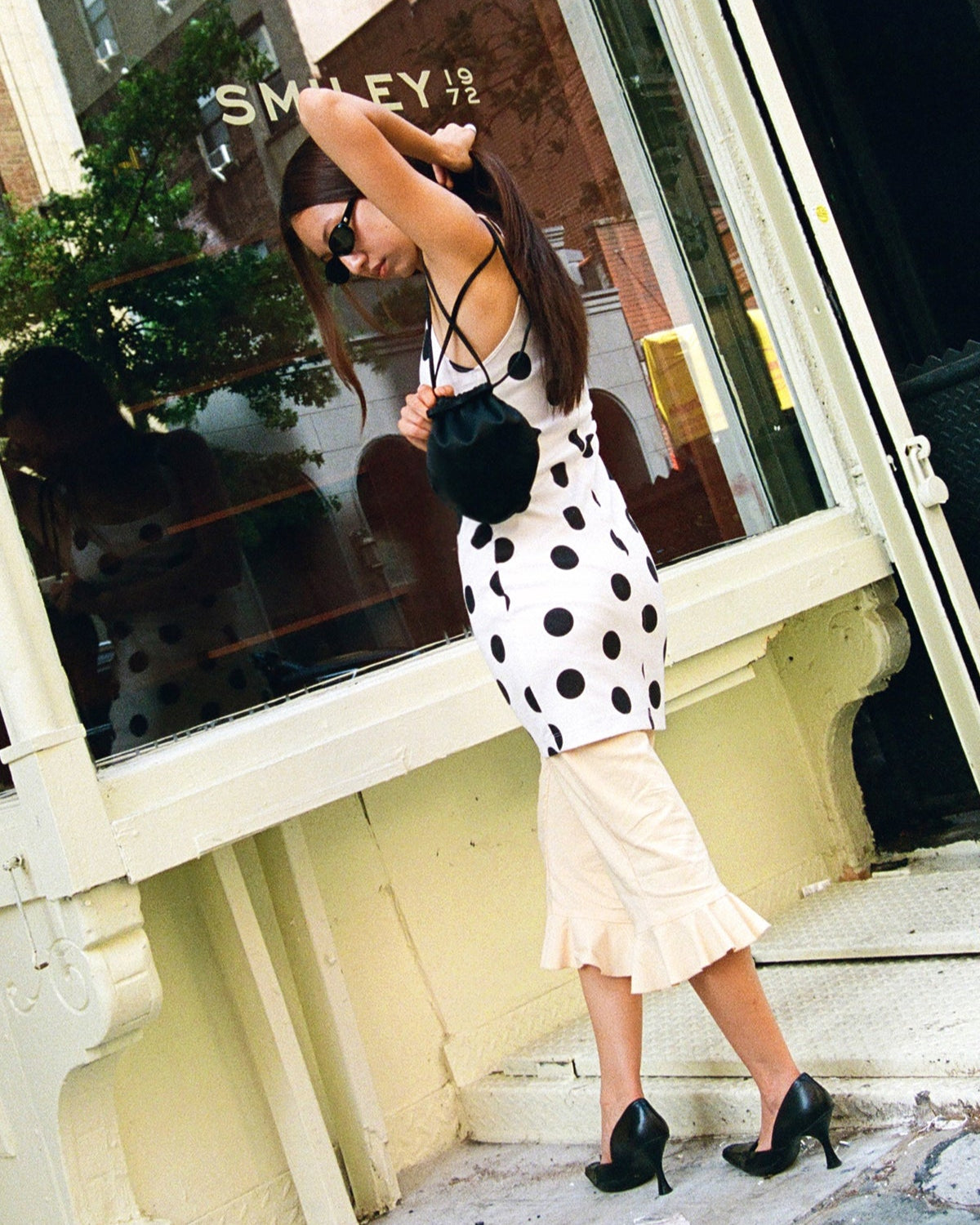 Woman in polka dot dress and black high heels standing on a city street.